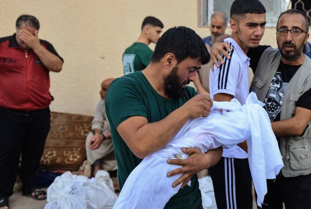 Seorang lelaki kelihatan sayu ketika membawa mayat anaknya di hadapan bilik mayat Hospital Al-Aqsa di Deir Balah di tengah Semenanjung Gaza, berikutan serangan Israel pada Ahad. - Foto AFP