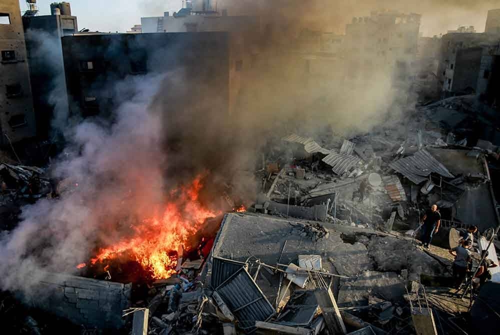 Penduduk Palestin berdiri di atas runtuhan bangunan ketika asap dan api meningkat daripada kemusnahan berikutan serangan Israel di Gaza City. Foto AFP