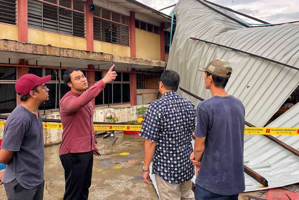 Chee Yee (dua dari kiri) melihat keadaan bumbung SMK Munshi Abdullah yang diterbangkan angin.