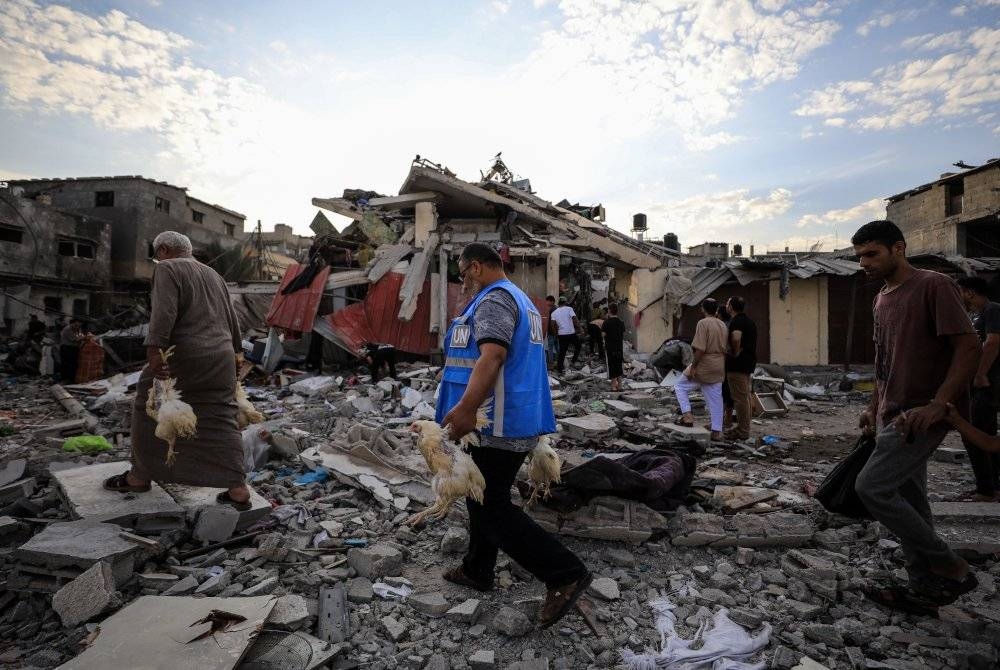 Orang ramai berjalan di antara rumah yang rosak selepas serangan udara Israel di selatan Semenanjung Gaza. - Foto Xinhua