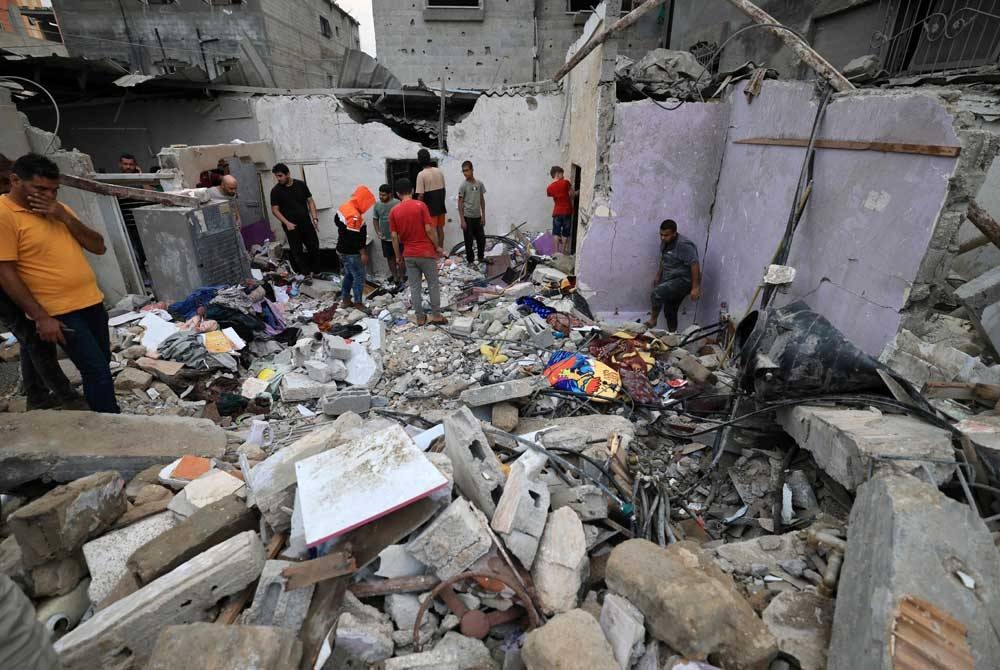 Orang ramai memeriksa kerosakan bangunan selepas serangan Israel ke atas Khan Yunis di selatan Semenanjung Gaza. - Foto MAHMUD HAMS/AFP