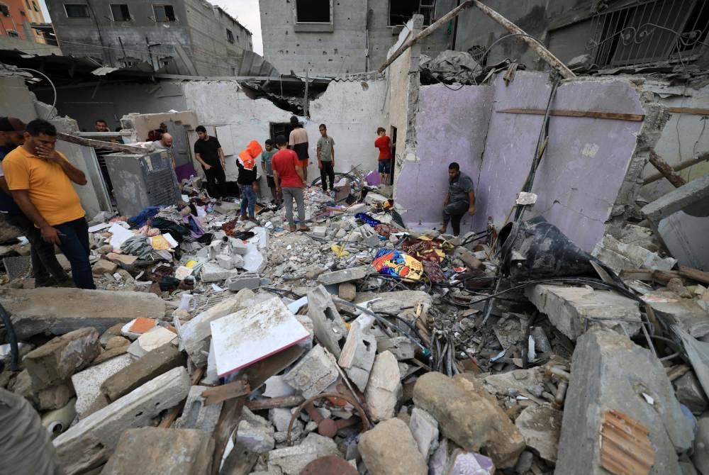 Orang ramai memeriksa kerosakan bangunan selepas serangan Israel ke atas Khan Yunis di selatan Semenanjung Gaza. - Foto MAHMUD HAMS/AFP