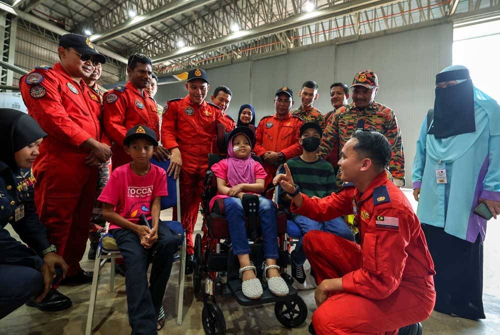 Timbalan Komander I Pangkalan Udara Wilayah Utara Jabatan Bomba dan Penyelamat Malaysia (JBPM) Penguasa Kanan Bomba II Muhammad Fisol Rosli (depan) berbual mesra dengan Nurul Umairah Abd Rahman, 9 (tengah), Muhamad Firas Haziq Samsol, 9 (kiri) serta Muhamad Yazeed Muhamad Yamin, 15 (kanan) yang mengidap kanser pada program menunaikan impian mereka, pada Khamis. Foto Bernama