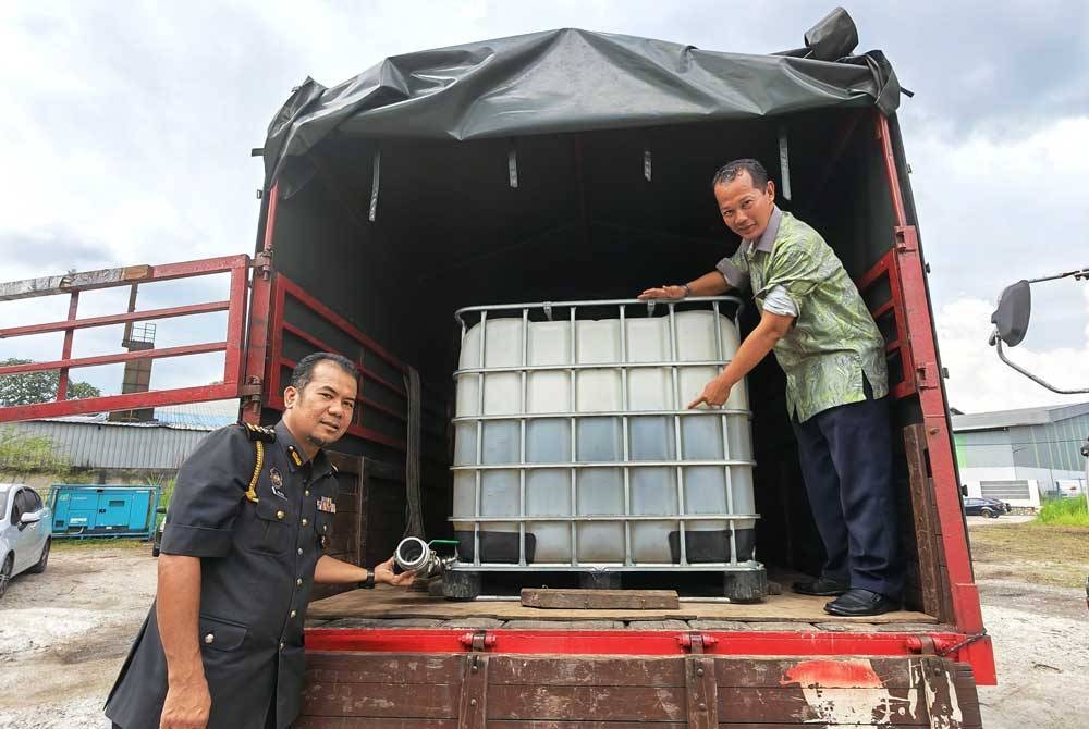 Muhammad Zahir (kanan) menunjukkan tangki IBC berisi diesel yang dirampas dalam serbuan di Negeri Sembilan.