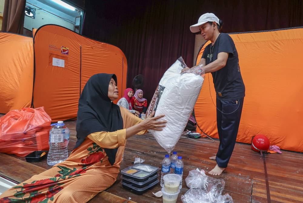 Pasah (kanan) tidak membataskan pergerakan dan aktivitinya dalam membantu mangsa banjir lain di PPS SMK Dengkil pada Isnin. - Foto Bernama