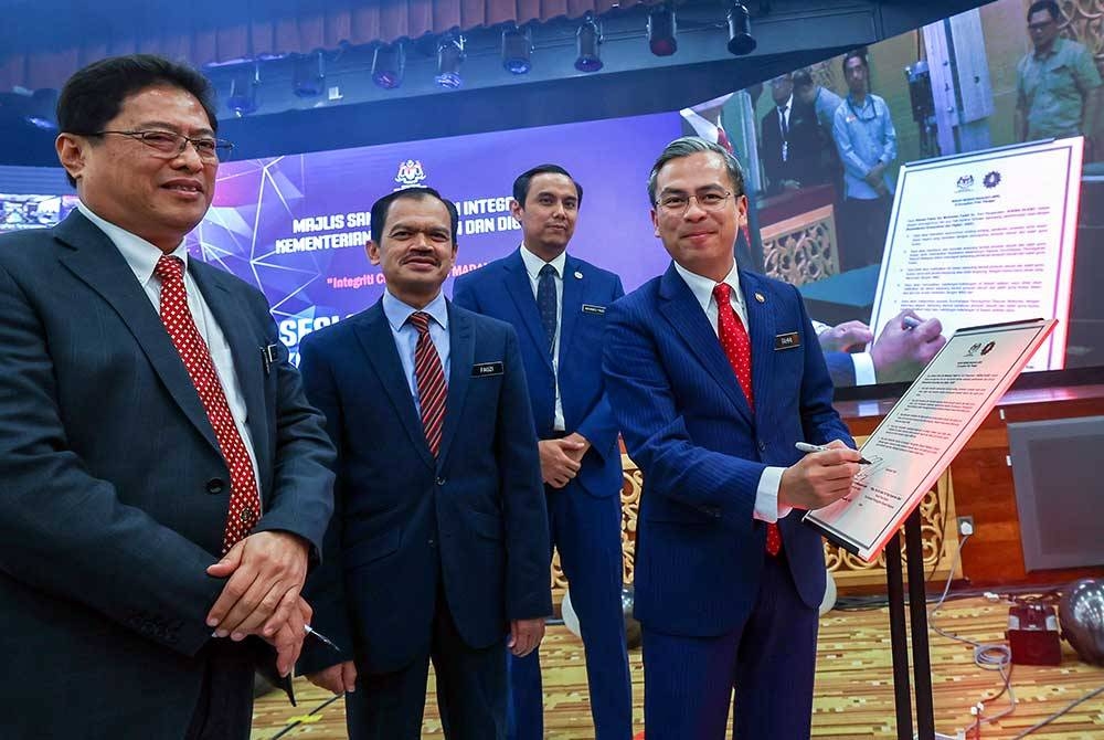 Menteri Komunikasi dan Digital, Fahmi Fadzil menandatangani Ikrar Bebas Rasuah sambil disaksikan oleh Azam (kiri) pada majlis sambutan Hari Integriti Kementerian Komunikasi dan Digital (KKD) bertemakan &#039;Integriti Citra Malaysia Madani&#039; di KKD,pada Selasa. - Foto Bernama