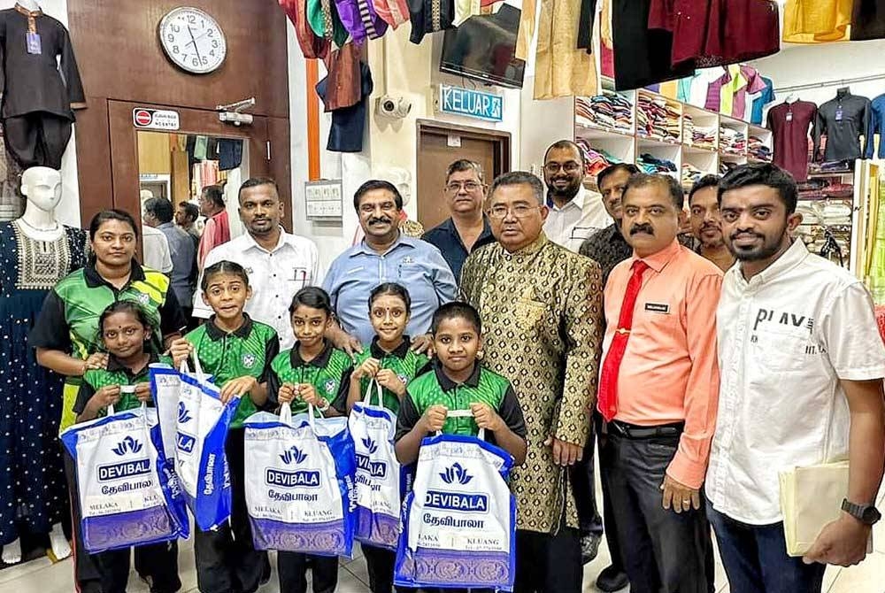 Karim (tiga dari kanan) dan Shanmugam (tiga dari kiri) bersama sebahagian pelajar yang menerima sumbangan pakaian raya di Little India, Jalan Bendahara di sini, pada Rabu.