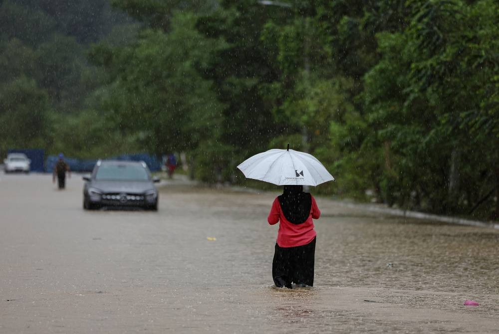 Penduduk D'Aman Meru Raya melintasi jalan yang dinaiki air ketika tinjauan di Meru Raya pada Isnin. - Foto Bernama