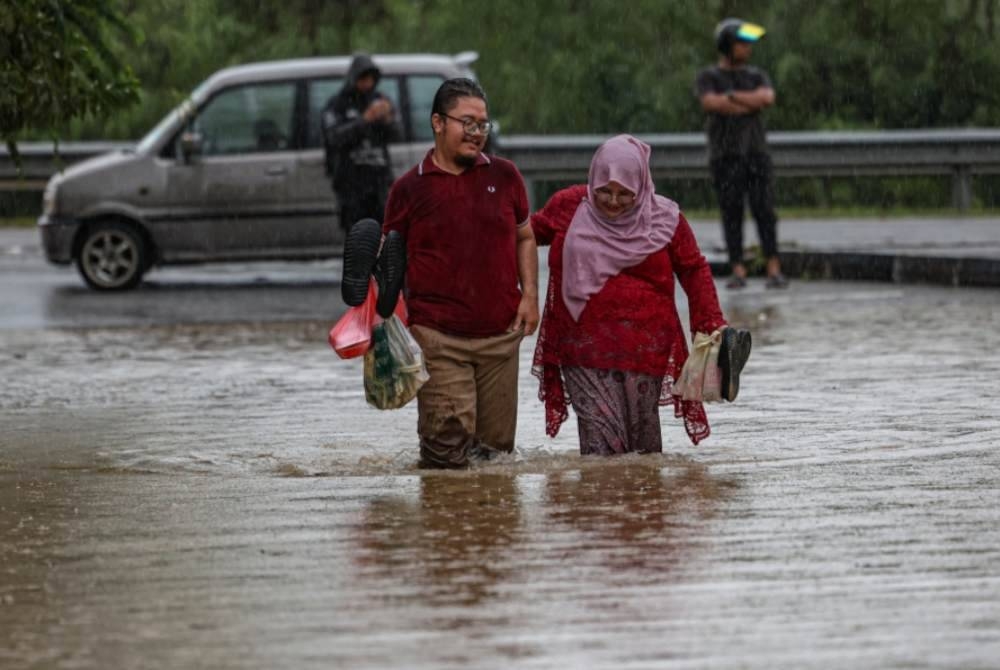 Penduduk D&#039;Aman Meru Raya melintasi jalan yang dinaiki air ketika tinjauan di Meru Raya. - Foto Bernama