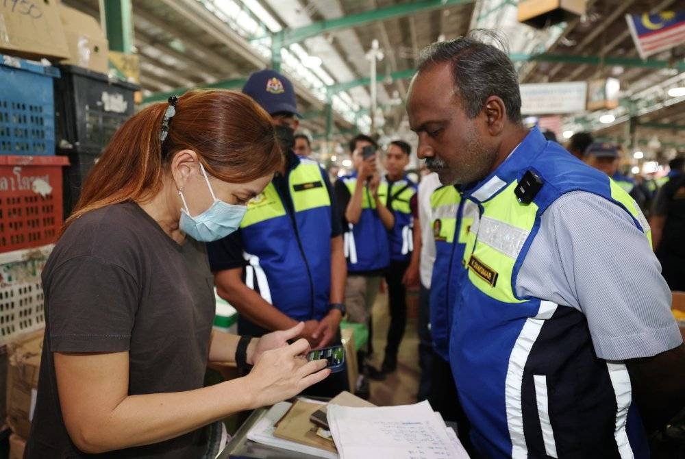 Sivakumar memeriksa majikan mengenai status pekerja melalui telefon pintar mereka ketika mengetuai Ops Bersepadu di Pasar Borong Kuala Lumpur pada Rabu. - Foto Bernama