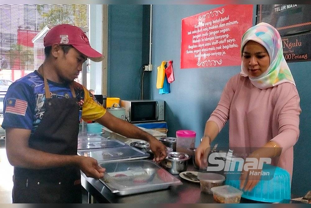 Nor Solihah (kanan) bersama pekerja menyusun bekas berisi lauk di restoran miliknya di Indera Mahkota pada Rabu.