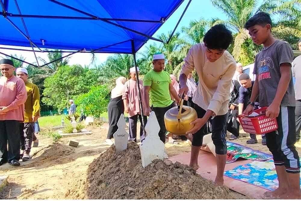 Ehmad Hadie Elfardie (dua dari kanan) dan Salman Elkhoyri (kanan) menyiram air ke pusara ayah mereka.