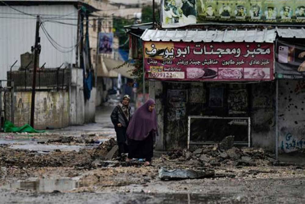 Rakyat Palestin berjalan di kawasan yang dimusnahkan tentera rejim Zionis Israel ketika operasi di kem pelarian Jenin. - Foto AP