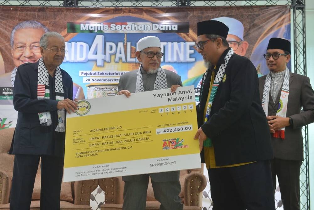 Abdul Hadi (tengah) sambil disaksikan Dr Mahathir (kiri) menerima replika cek bagi dana Aid4Palestin 2.0 daripada wakil badan bukan kerajaan (NGO) pada majlis penyerahan di Cyberjaya pada Isnin.