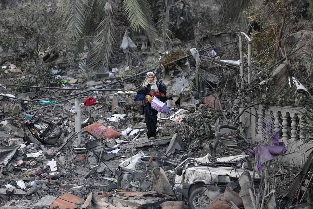 Wanita Palestin berjalan di celah runtuhan dan kemusnahan di bandar Gaza akibat kekejaman Israel. - Foto AFP