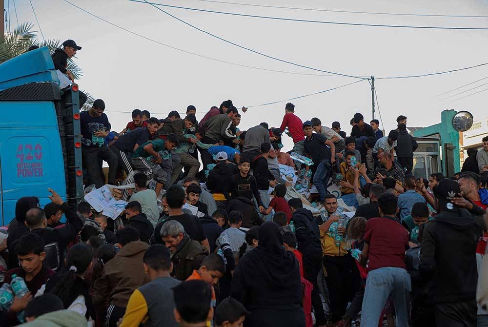 Rakyat Palestin mendapatkan air minuman daripada trak yang sarat dengan bekalan makanan di bandar Khan Younis, selatan Semenanjung Gaza. - Foto Xinhua