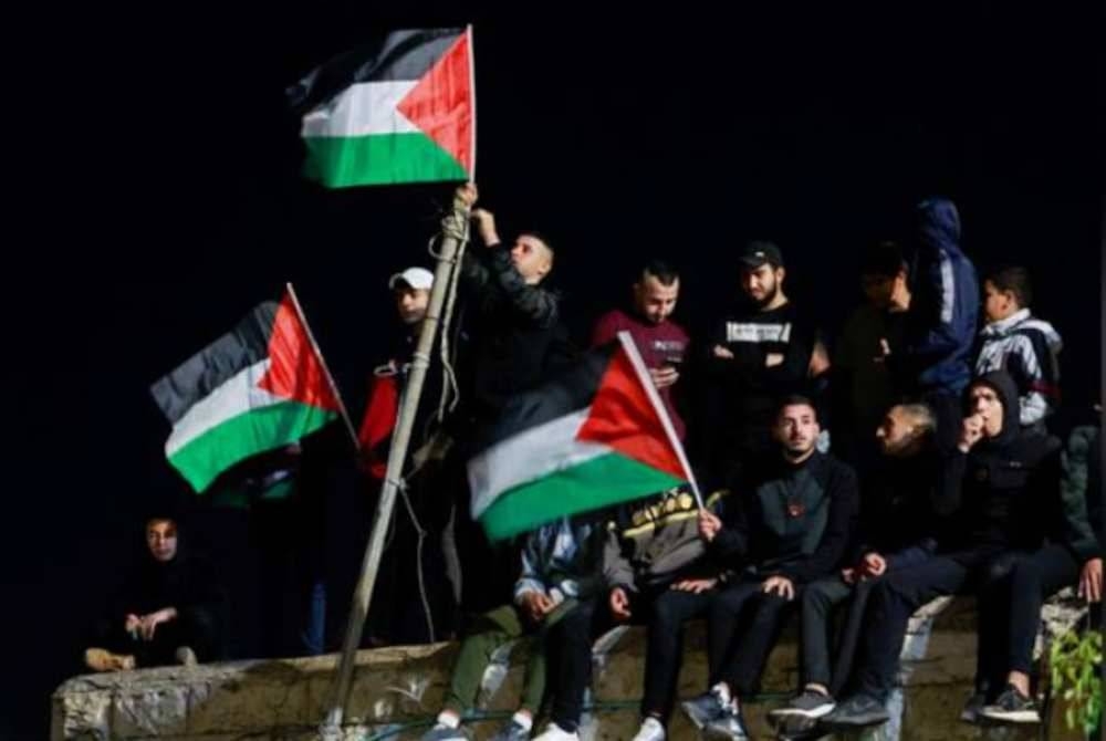 Rakyat Palestin mengibarkan bendera negara itu ketika tahanan dibebaskan dari penjara Israel. - Foto REUTERS