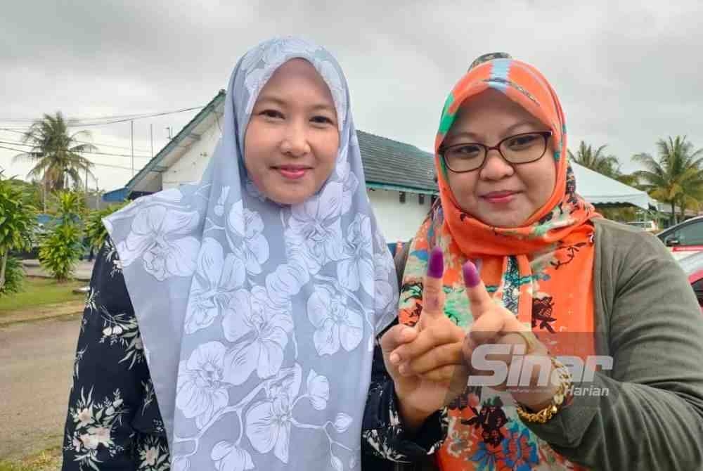 Norhayati Ismail (kiri) dan Razidah Razali (kanan) menunjukkan jari selepas menunaikan tanggungjawab di pusat mengundi awal Balai Polis Kijal, Kemaman pada Selasa.