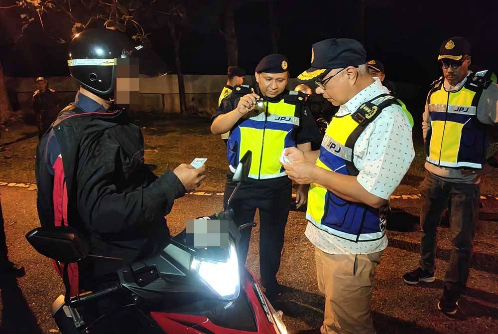 Lokman (kanan) memeriksa lesen seorang penunggang motosikal ketika Ops Patuh di tol Senawang.