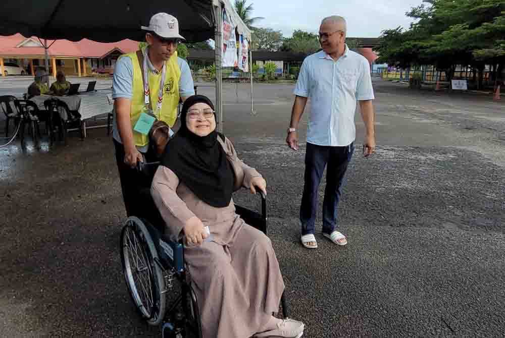 Kasmani yang ditemani suaminya dan dibantu petugas SPR bagi memudahkan pergerakan ketika mengundi bagi PRK Kemaman pada Sabtu.