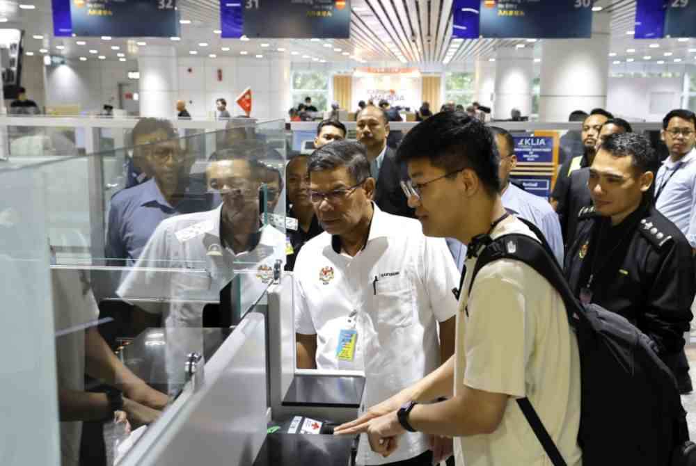 Saifuddin Nasution melihat seorang pelancong melalui tempat pemeriksaan pasport semasa melihat proses pelaksanaan Pelan Liberalisasi Visa di KLIA Terminal 1 pada Selasa. - Foto Bernama