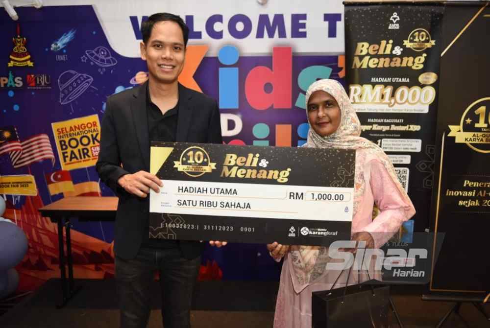 Izzat Izhar (kiri) menyampaikan hadiah utama RM1000 kepada Norsham (kanan) ketika program Kempen Beli & Menang 10 tahun al-Quran Karya Bestari. - Foto Sinar Harian MOHD RAFIQ REDZUAN HAMZAH.