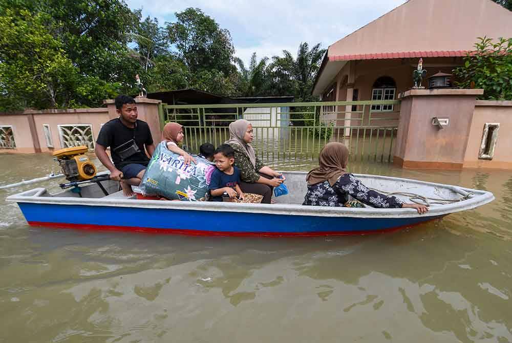 Pemandu bot, Raihan Mohamad, 24, (kiri) membantu memindahkan penduduk dari Kampung Serongga ke PPS Sekolah Kebangsaan Sri Kiambang berikutan kediaman mereka dilanda banjir. - Foto Bernama