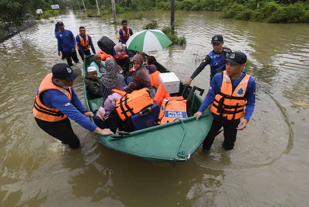 Anggota polis Ibu Pejabat Polis Daerah (IPD) Pasir Mas membantu memindahkan penduduk Kampung Serongga ke PPS Sekolah Kebangsaan Sri Kiambang berikutan kediaman mereka dilanda banjir. - Foto Bernama