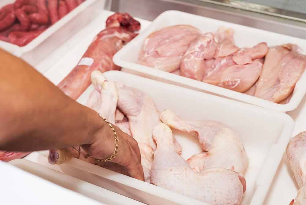 Butcher serving fresh chicken meat at display in butchery