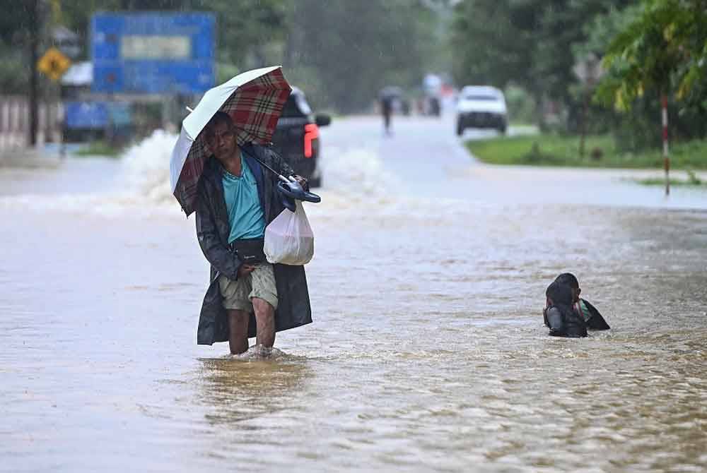 Penduduk meredah banjir untuk ke Pusat Pemindahan Sementara (PPS) selepas kawasan rumah mereka dinaiki air ketika tinjauan di Kampung Pengkalan Ajal hari ini. - Foto: Bernama