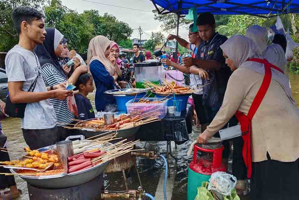 Saida (kanan) tidak menang tangan melayan permintaan pelanggan yang mahu membeli makanan proses yang dijualnya di Kampung Pohon Tanjong di Pasir Mas. - Foto Bernama