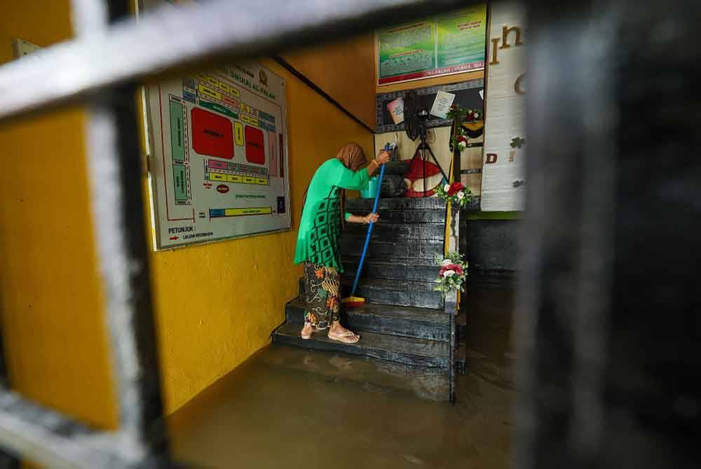 Rugayah membersihkan kesan lumpur pada tangga sekolah disebabkan banjir yang berlaku sejak 26 Disember lalu di Sekolah Menengah Ugama (Arab) Al-Falah di Kampung Siram. - Foto: Bernama