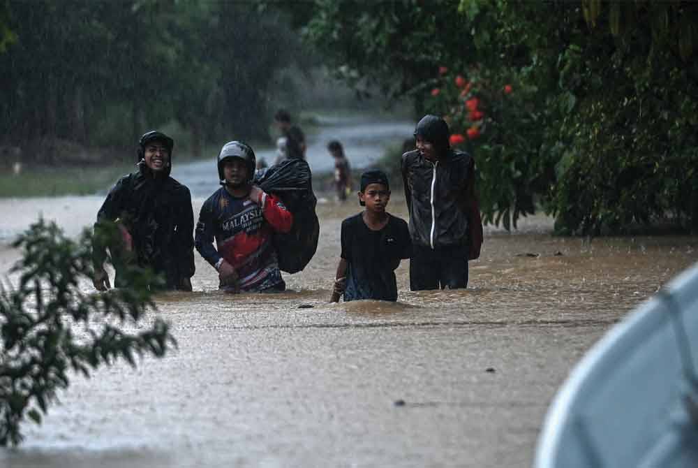 Penduduk meredah air bah dengan membawa barangan keperluan untuk ke tempat lebih selamat selepas kawasan berkenaan dinaiki air ketika tinjauan di Kampung Belimbing Jongok Batu, Dungun pada 25 Disember lalu. - Foto: Bernama