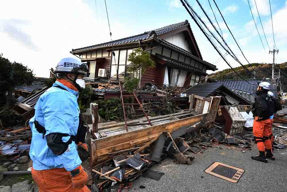 Anggota bomba memeriksa rumah kayu yang runtuh di bandar Wajima
selepas gempa bumi kuat melanda Jepun pada Isnin. - Foto AFP