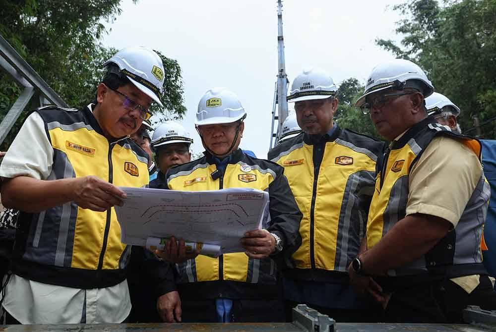 Alexander Nanta Linggi (tengah) diberi penerangan oleh Pengarah Cawangan Senggara Fasiliti Jalan JKR, Ir Mohd Nasir Bontat (kiri) ketika meninjau pemasangan jambatan Panel Keluli Bermodular (Bailey Bridge) di kawasan kejadian jalan mendap di laluan FT66 Seksyen 73.850 Jalan Dabong-Jeli hari ini. Foto Bernama