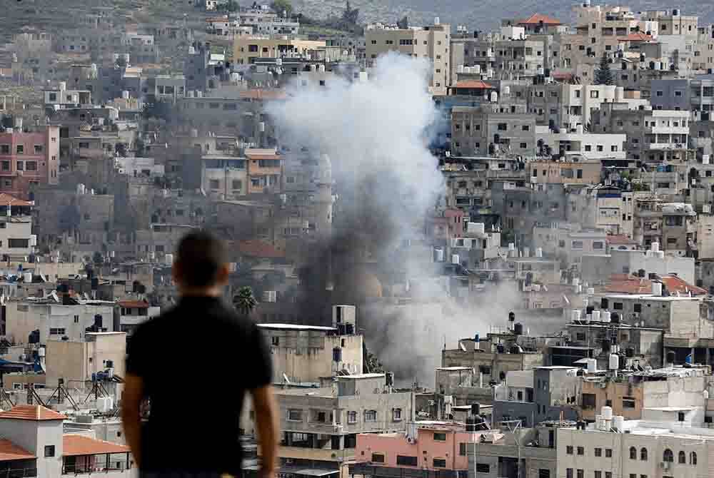 Seorang lelaki melihat kepulan asap atas bangunan kem Nur Syams di Tebing Barat yang diserbu tentera Israel. Foto AFP