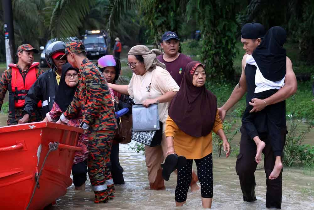 Anggota Jabatan Bomba dan Penyelamat Malaysia (JBPM) membantu memindahkan penduduk Kampung Batu 20 dan Kampung Bukit Dagang, Sungai Tiram yang terputus hubungan selepas jalan utama memasuki perkampungan itu dinaiki air akibat limpahan air sungai berdekatan pada Ahad. Foto Bernama