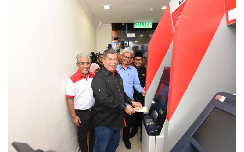 Mohamad (depan) membuat transaksi di mesin pengeluaran wang automatik (ATM) di Pusat Pembangunan Komuniti atau Community Development Centre (CDC) Agrobank di RTC Tunjung, Kota Bharu pada Selasa. 