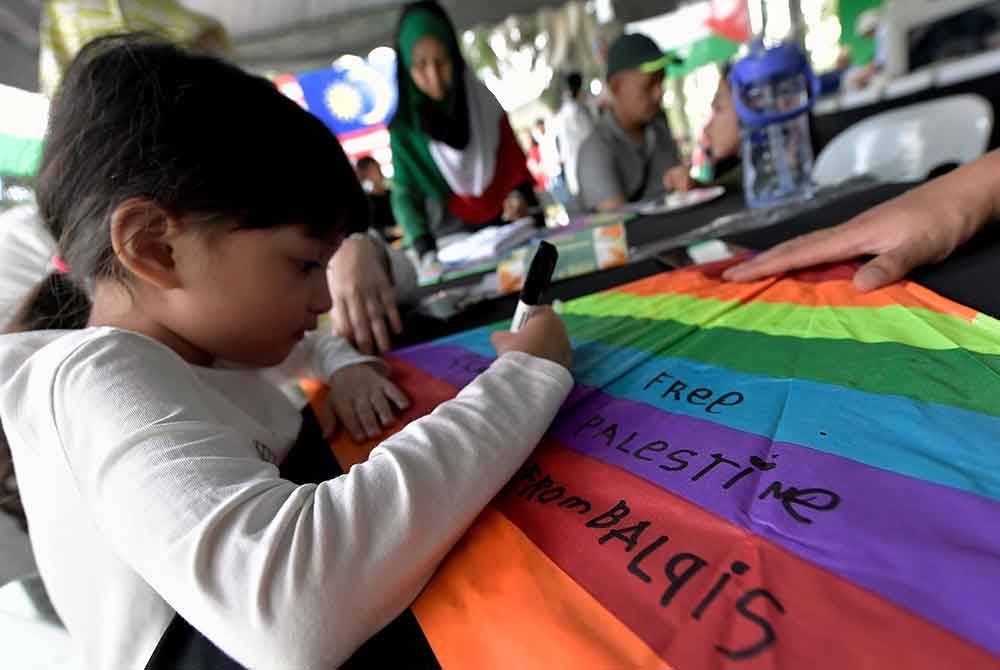 Peserta cilik menulis 'Free Palestine' di atas layang-layangnya ketika menyertai aktiviti 'Fly Kite for Gaza' di MST Golf Driving Range @ Bukit Jelutong Golf Centre pada Ahad. Foto Bernama