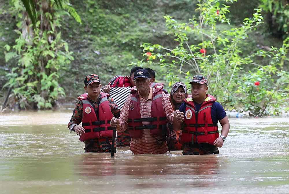 Anggota Bomba dan Penyelamat membantu warga emas Dockery Raymond, 75, (tengah) dan isterinya Puan Rahilah, 68, (dua dari kanan) meredah banjir untuk dipindahkan ke PPS selepas rumah mereka terputus hubungan akibat banjir di Kampung Rancangan Cocos, Belurun. Foto Bernama