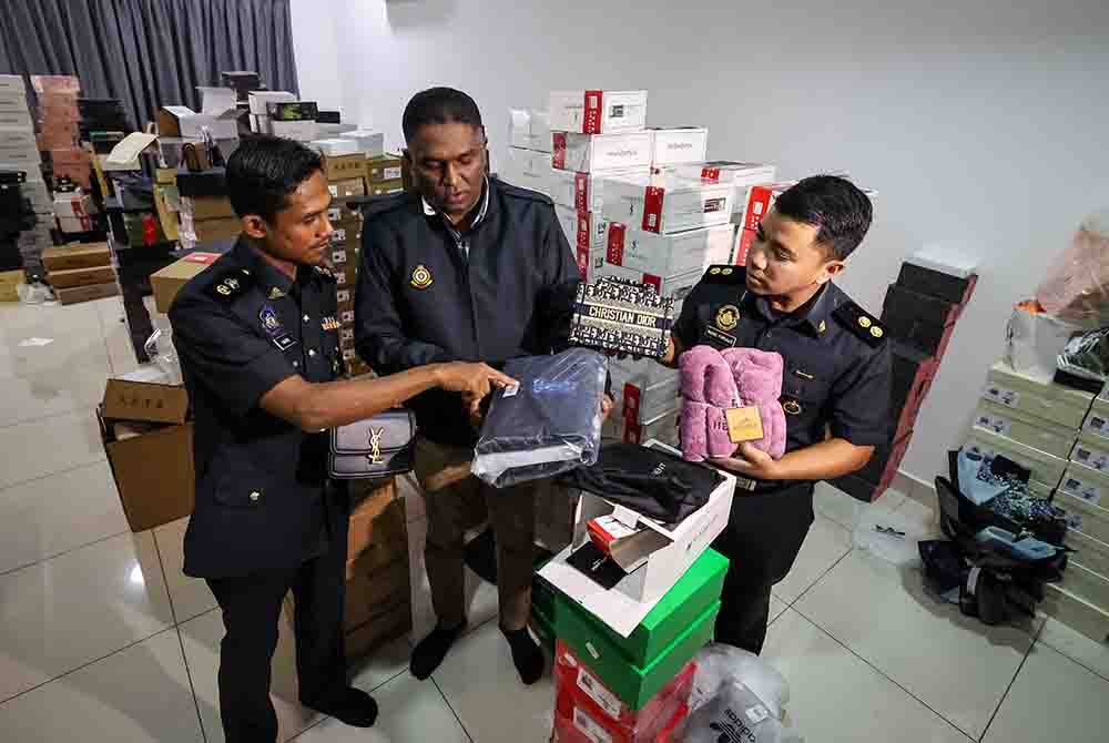 Jegan (tengah) bersama pegawainya menunjukkan pelbagai barangan berjenama tiruan yang dirampas dalam satu serbuan di sebuah premis dekat Simpang Ampat pada Isnin. Foto Bernama