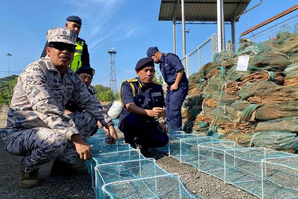 Wan Muhammad Aznan ( kanan) dan Romli (kiri) menunjukkan sebahagian bubu naga dirampas dalam operasi khas sekitar perairan Kedah dalam operasi sejak Isnin.