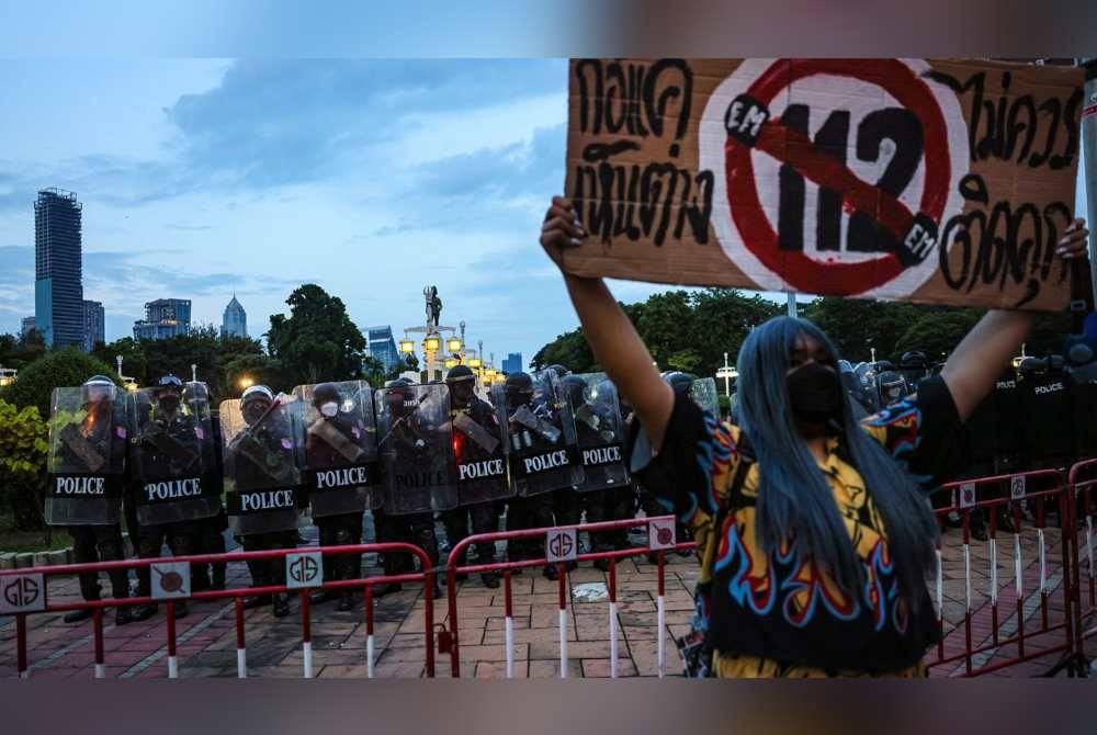 Seorang penunjuk perasan memakai pelitup muka sambil memegang poster tertera nombor 112 yang merujuk kepada undang-undang lese-majeste ketika demonstrasi di Bangkok pada November 2021. Agensi