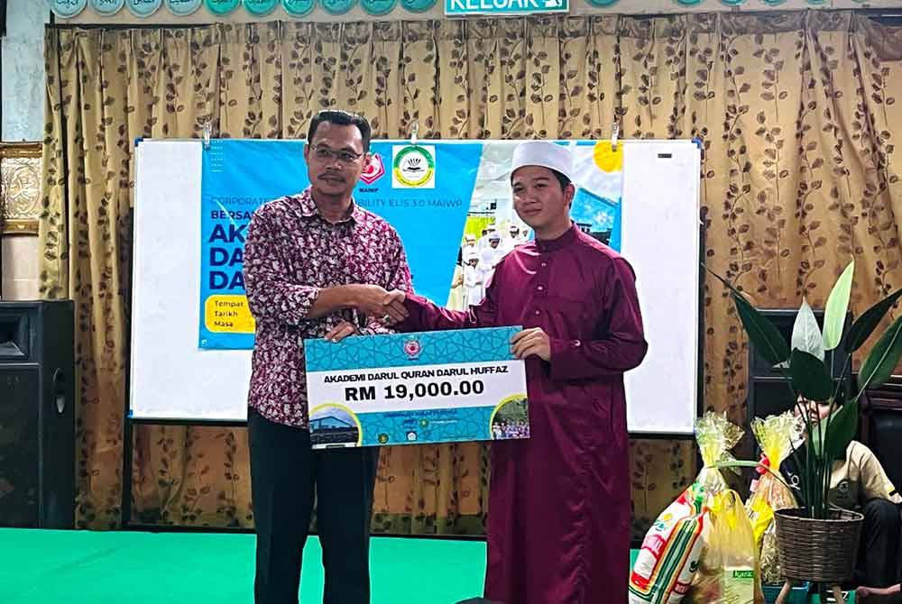 Mohd Fauzi (kiri) menyerahkan sumbangan RM19,000 kepada Ahmad Fakhrur Razi kepada Akademi Darul Quran Darul Huffaz Kampar sempena Program Tanggungjawab Sosial Korporat (CSR) Bersama Akademi Darul Quran Darul Huffaz di Taman Bandar Baru, di sini pada Isnin. Foto MAIWP