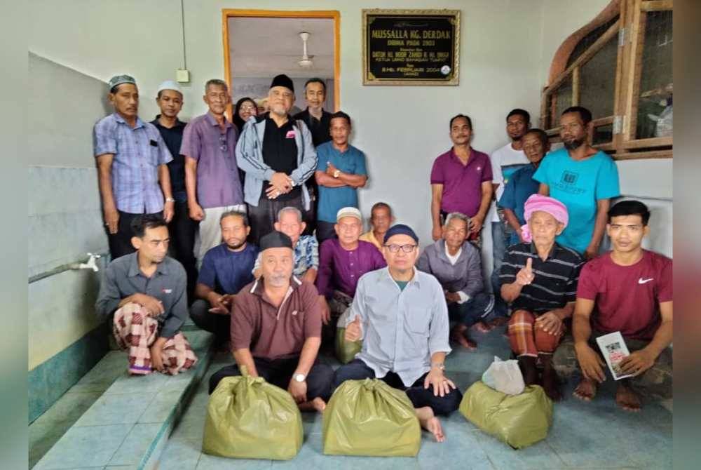 Aziz (berdiri, empat dari kiri) bersama sebahagian penduduk yang menerima sumbangan daripada OMIW.