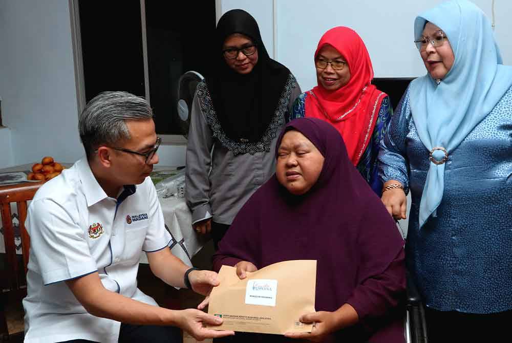 Fahmi (kiri) menyampaikan sumbangan kepada bekas Penerbit Rancangan RTM Melaka, Norazlin Mohamad, 52, di Kampung Pulai, Merlimau hari ini. Foto Bernama