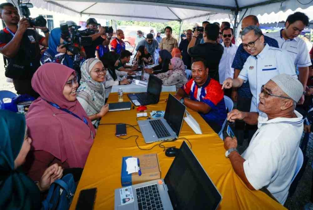 Menteri Komunikasi, Fahmi Fadzil (kanan) beramah mesra dengan penduduk setempat yang sedang mendaftar akaun dalam Pangkalan Data Utama (PADU) pada Program Jiwa MADANI di Kampung Sungai Putat dekat Ayer Keroh pada Sabtu. Foto Bernama