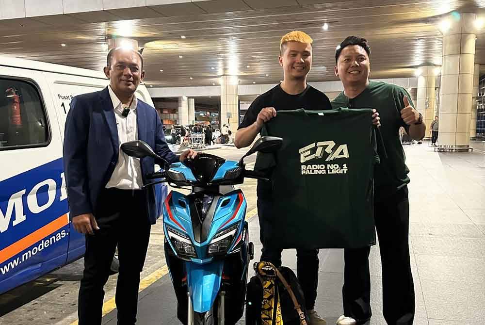 Derrick (tengah) bersama jentera yang disumbangkan Modenas di KLIA. Foto Modenas