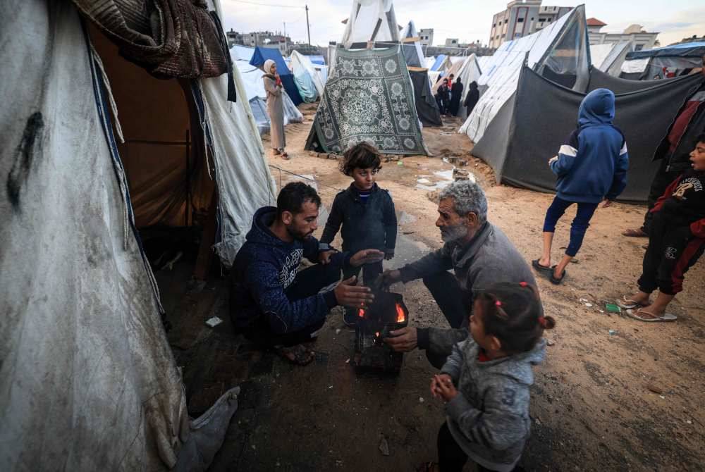 Penduduk Palestin yang dipindahkan cuba memanaskan badan di tengah-tengah khemah yang dibanjiri hujan lebat, di kem sementara di tengah-tengah pertempuran antara tentera Israel dan pejuang Hamas. Foto AFP