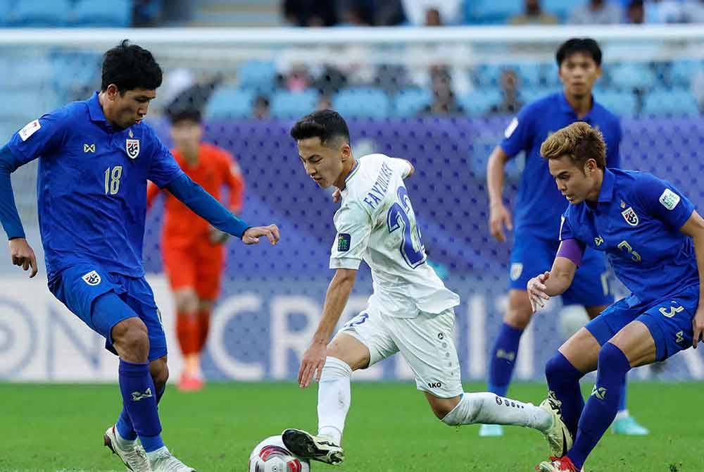 Abbosbek Fayzullaev cuba melepasi kawalan pemain Thailand pada pusingan kalah mati di Stadium Al Janoub. - AFP